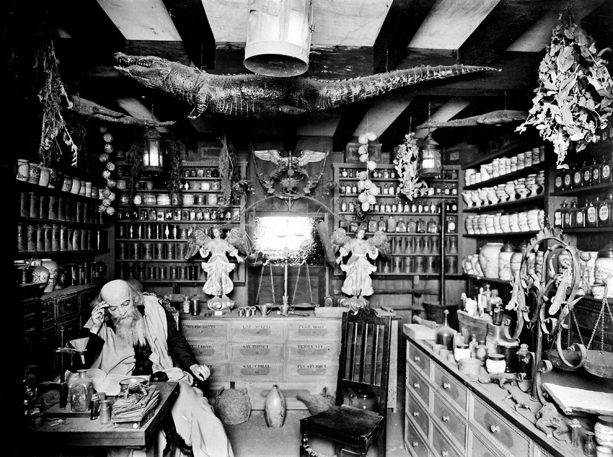 Reconstruction of a seventeenth-century apothecary's shop: a bearded pharmacist reads at a desk surrounded by jars, scales, and a stuffed crocodile hung from the ceiling